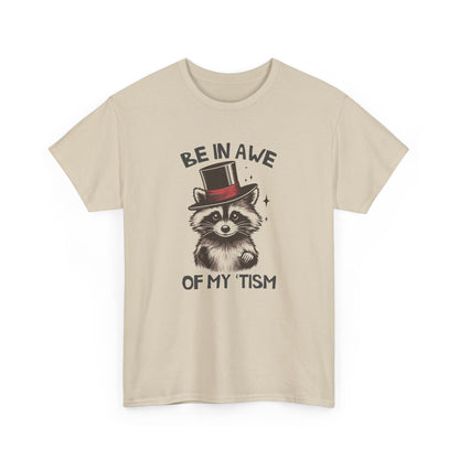 Front view of a beige T-shirt featuring a raccoon wearing a top hat with the text "Be In Awe Of My Tism." Part of the Vivid Divergence Sensory Friendly Unisex Tees Range.