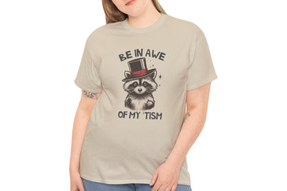 Model wearing a beige T-shirt featuring a raccoon with a top hat and the text "Be In Awe Of My Tism," shown from the front. Part of the Vivid Divergence Sensory Friendly Unisex Tees Range.