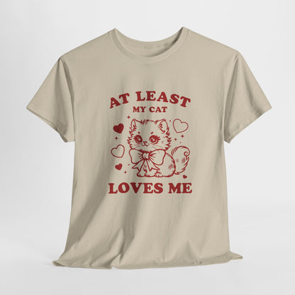 Hanging view of a beige T-shirt with red text and cat illustration that reads "At Least My Cat Loves Me." Exclusive release for Valentine’s Day. Part of the Vivid Divergence Sensory Friendly Unisex Tees Range.