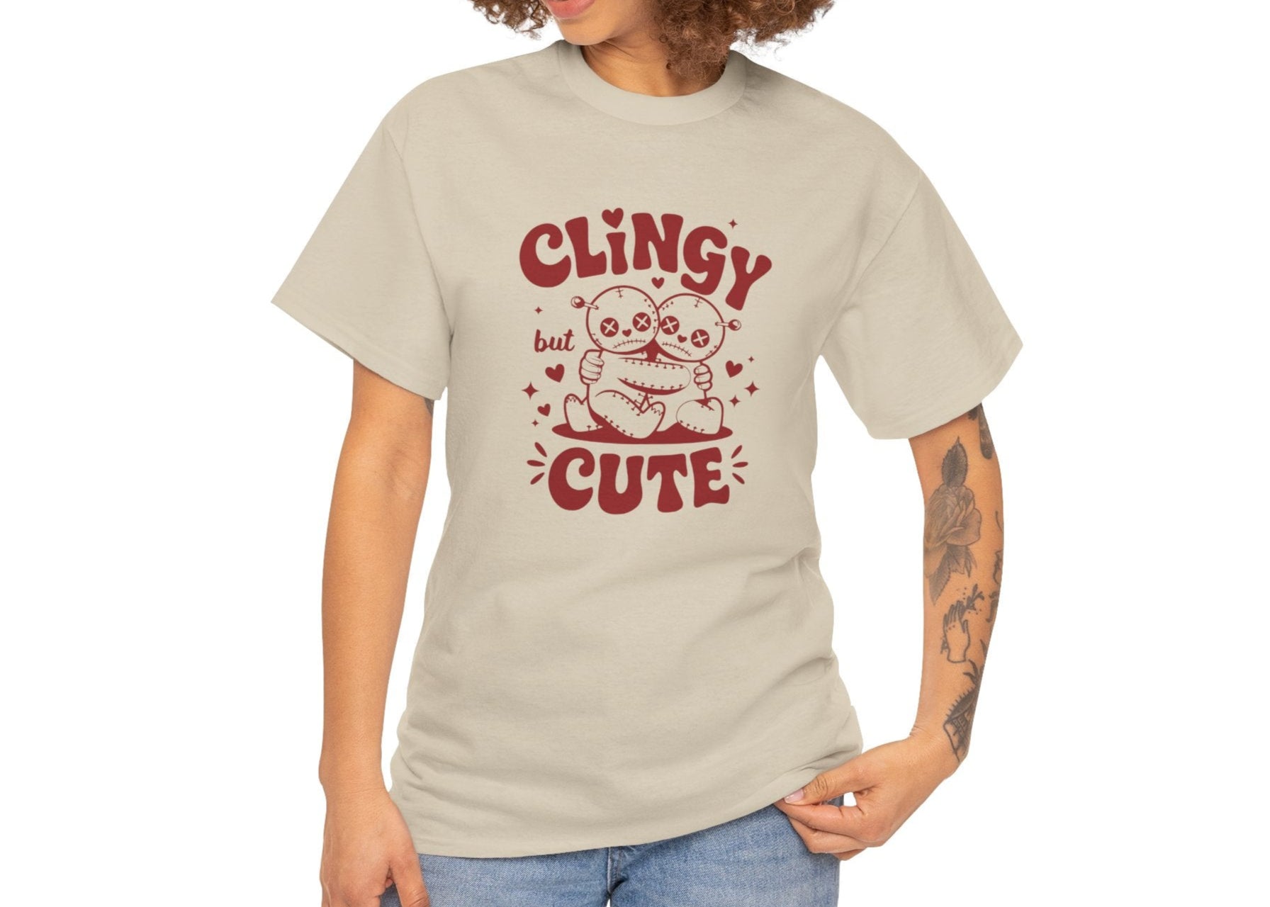 Woman with curly hair wearing a beige T-shirt with red text and cartoon sloth illustration that reads "Clingy But Cute." Exclusive release for Valentine’s Day. Part of the Vivid Divergence Sensory Friendly Unisex Tees Range.