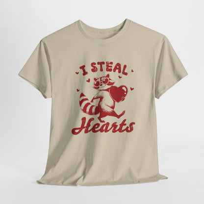 Hanging beige T-shirt with red text and raccoon illustration holding a heart that reads "I Steal Hearts." Exclusive release for Valentine’s Day. Part of the Vivid Divergence Sensory Friendly Unisex Tees Range.