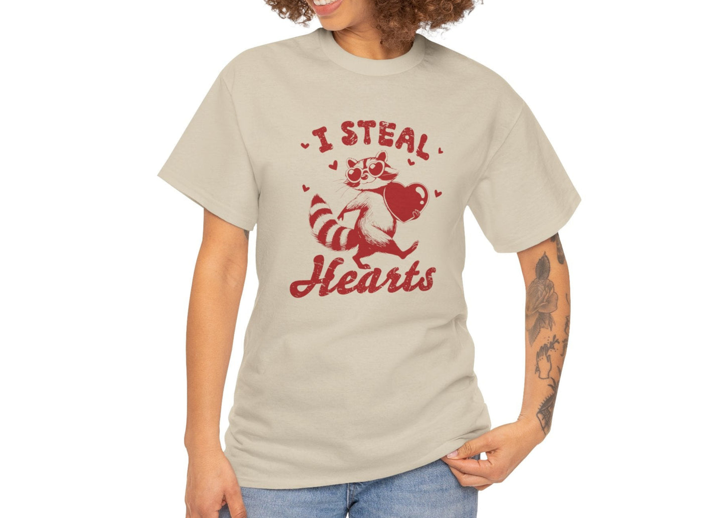 Woman with curly hair wearing a beige T-shirt with red text and raccoon illustration holding a heart that reads "I Steal Hearts." Exclusive release for Valentine’s Day. Part of the Vivid Divergence Sensory Friendly Unisex Tees Range.