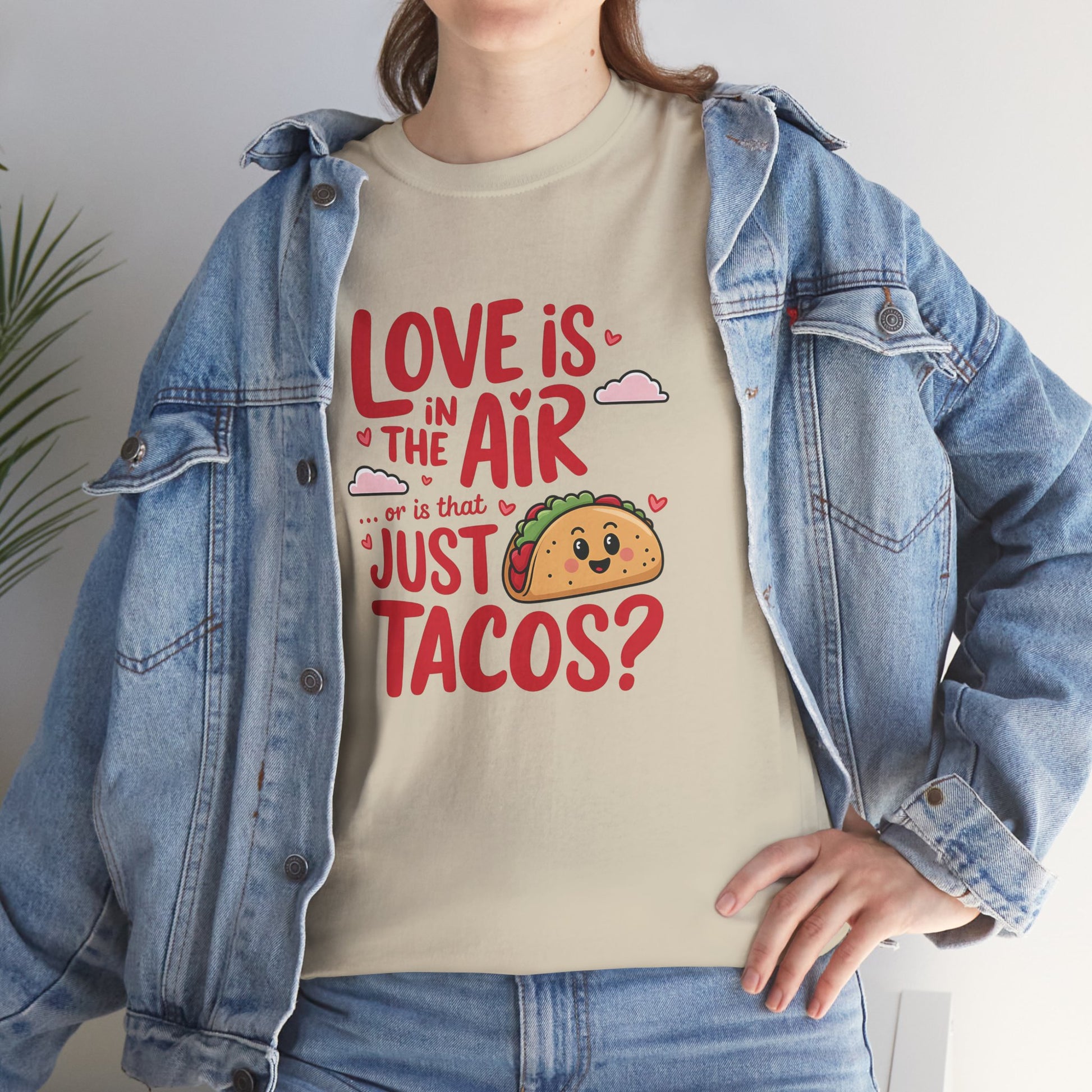 Front view of a woman wearing a beige T-shirt with a denim jacket, featuring red and black text with a taco illustration that reads "Love Is In The Air Or Is It Just Tacos?" Exclusive release for Valentine’s Day. Part of the Vivid Divergence Sensory Friendly Unisex Tees Range.