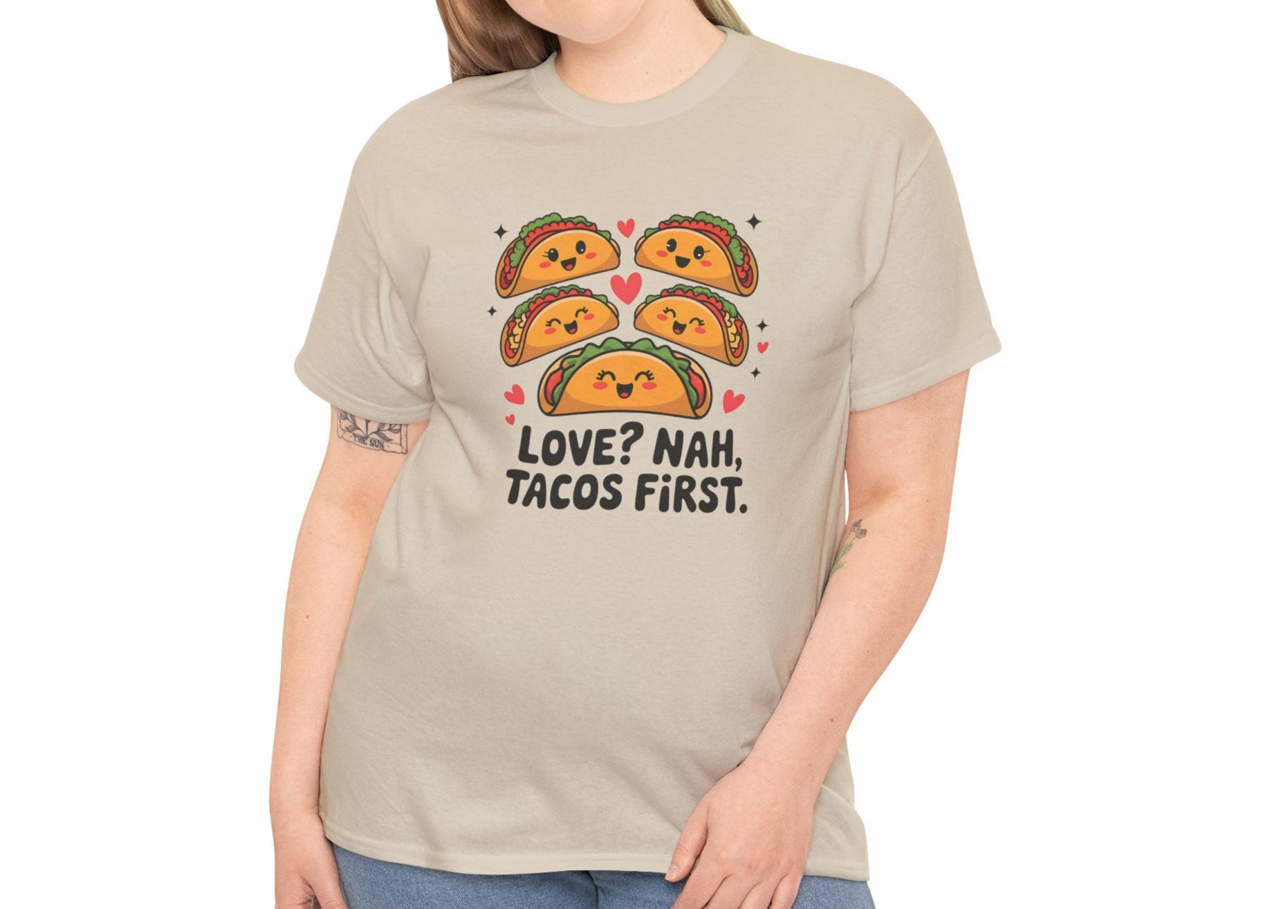 Front view of a beige T-shirt worn by a woman, featuring an illustration of tacos and black text that reads "Love? Nah, Tacos First." Exclusive release for Valentine’s Day. Part of the Vivid Divergence Sensory Friendly Unisex Tees Range.