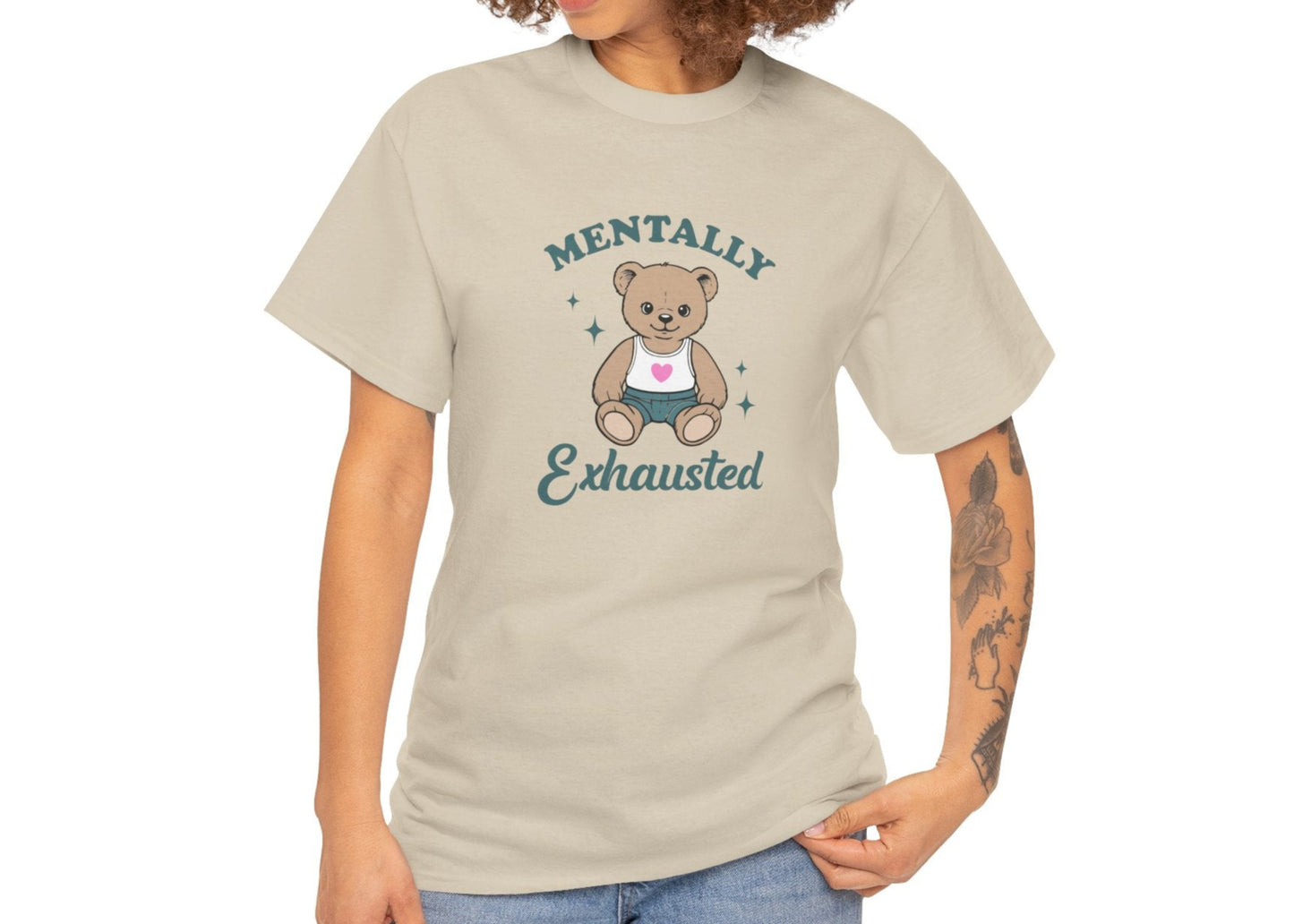 Modeled view of a beige T-shirt featuring a teddy bear graphic with the text "Mentally Exhausted." Part of the Vivid Divergence Sensory Friendly Unisex Tees Range.