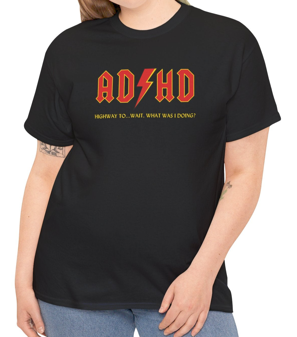 Model wearing a black T-shirt with orange "AD/HD" text, inspired by AC/DC, paired with jeans. Part of the Vivid Divergence Sensory Friendly Unisex Tees Range.