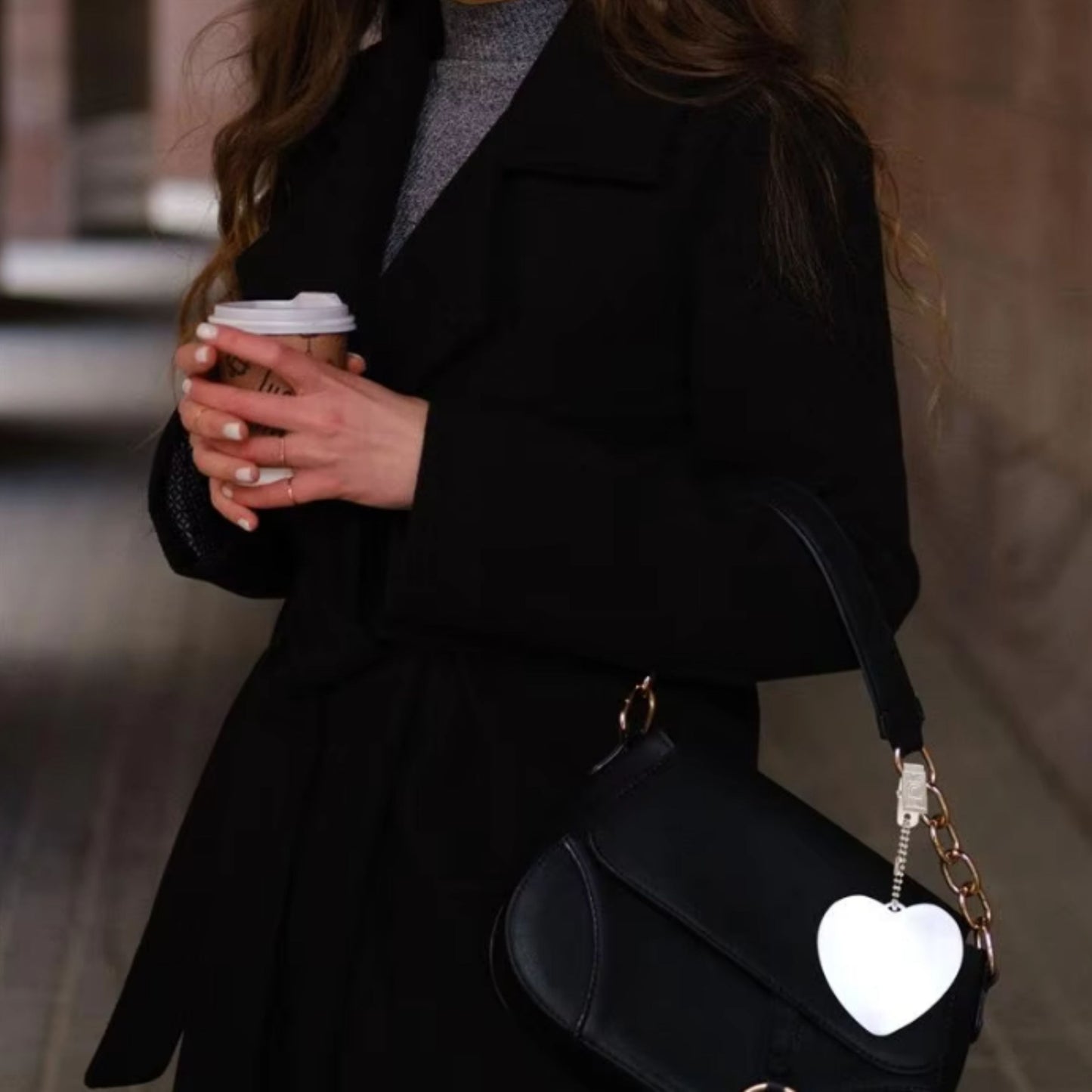  Woman holding a coffee cup with a black handbag featuring a heart-shaped LED bag clip, offering touch-activated illumination.