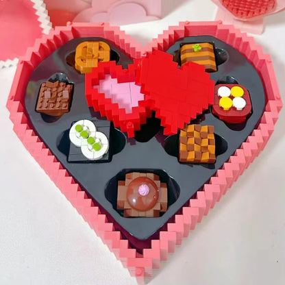 Assorted chocolate-themed building blocks inside a pink heart-shaped gift box with a red heart-shaped ring holder. 