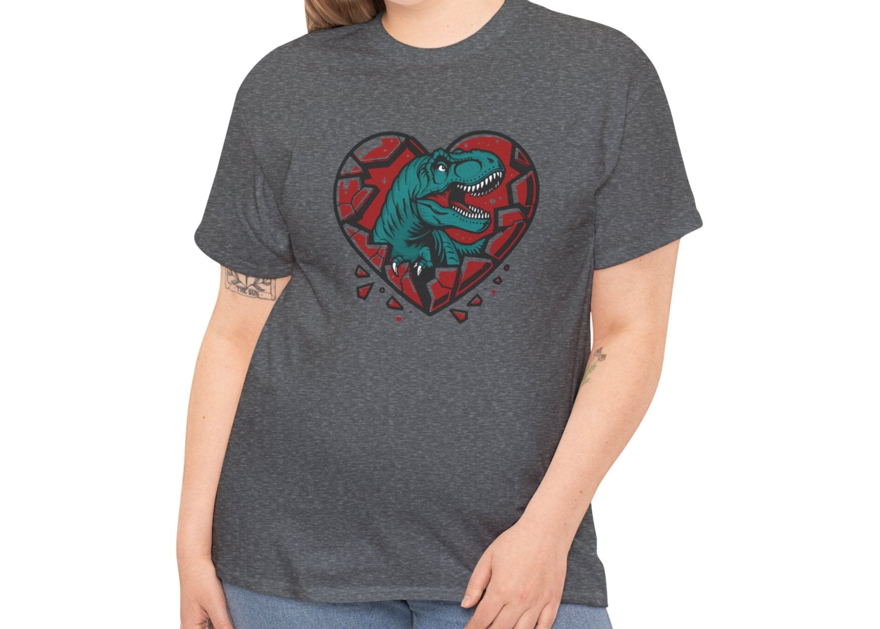 Woman wearing a dark gray T-shirt featuring a green dinosaur inside a cracked red heart with small black hearts around it. Exclusive release for Valentine’s Day. Part of the Vivid Divergence Sensory Friendly Unisex Tees Range.