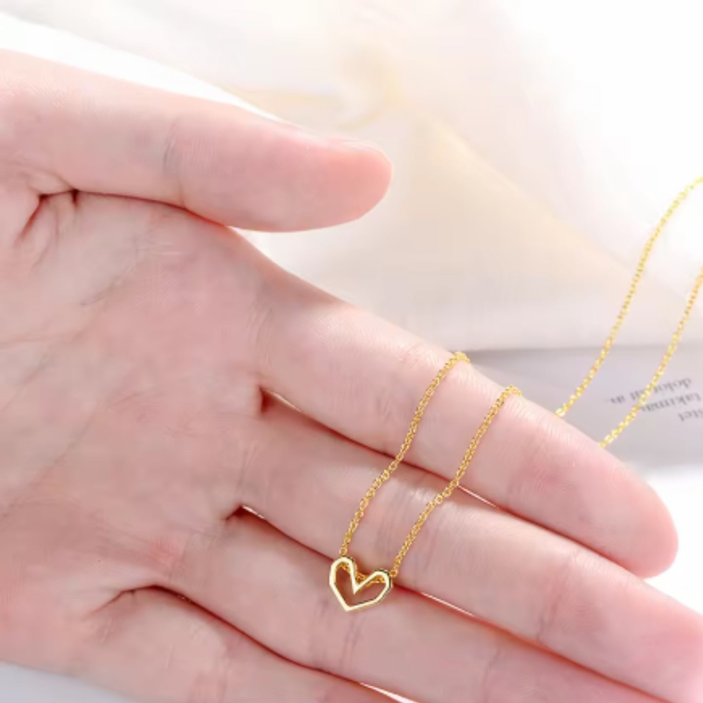  A gold geometric open heart necklace delicately displayed on an open hand, emphasizing its fine craftsmanship and dainty appearance.