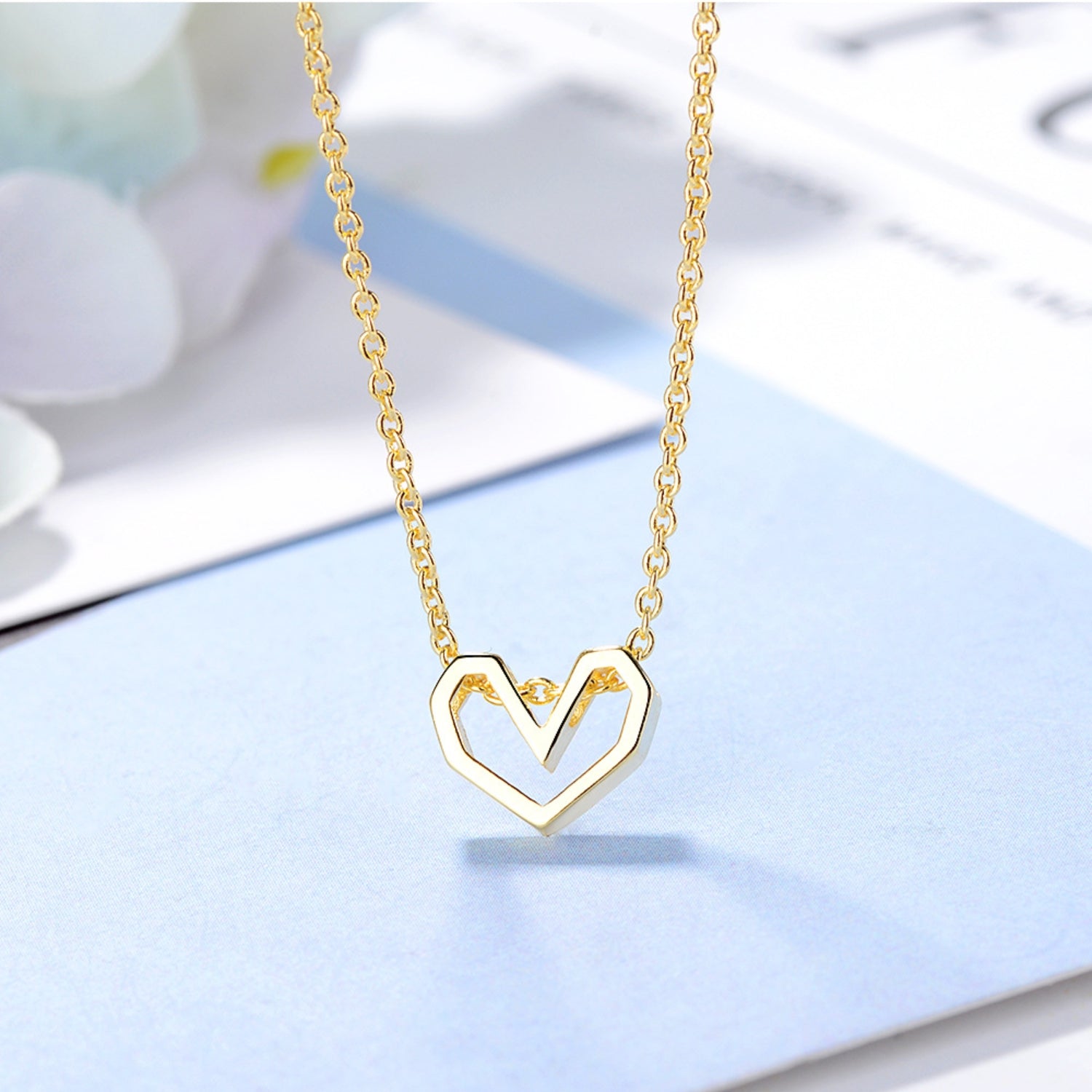 Gold geometric open heart necklace elegantly showcased on a light blue and white surface, accentuating its luxurious and modern design.