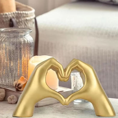 Gold hand-shaped sculpture forming a heart placed on a coffee table near candles. Stunning dopamine decor and a perfect gift for Valentine's Day.