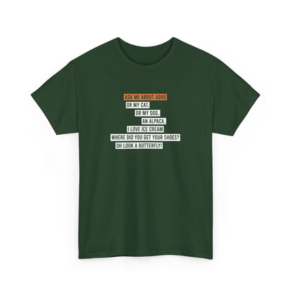 Front view of a green T-shirt displaying the text "Ask me about my ADHD, or my cat, or my dog, an alpaca, I love ice cream, Where did you get your shoes, oh look a butterfly" in white and orange. Part of the Vivid Divergence Sensory Friendly Unisex Tees Range.