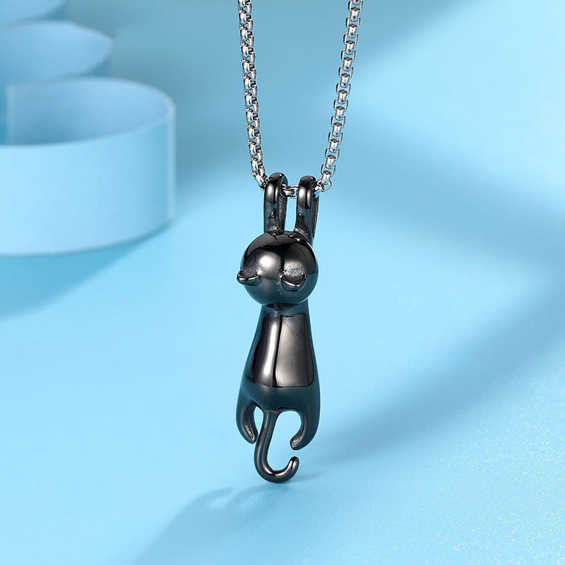 Close-up of the Hang Tight Cat Necklace in black titanium steel, highlighting its unique and whimsical design of a hanging cat, on a silver chain, shown on a light blue surface.