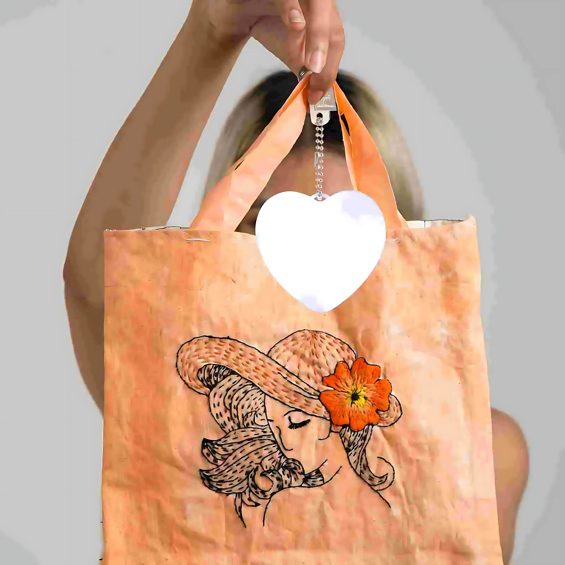 Heart-shaped LED bag clip attached to an orange tote bag with floral embroidery, showing its versatile clip-on feature.