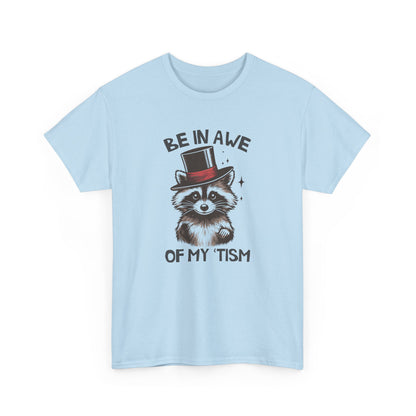 Front view of a light blue T-shirt featuring a raccoon wearing a top hat with the text "Be In Awe Of My Tism." Part of the Vivid Divergence Sensory Friendly Unisex Tees Range.