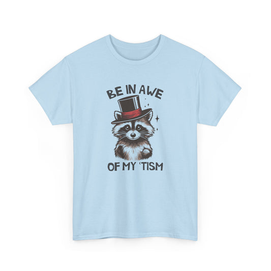 Front view of a light blue T-shirt featuring a raccoon wearing a top hat with the text "Be In Awe Of My Tism." Part of the Vivid Divergence Sensory Friendly Unisex Tees Range.