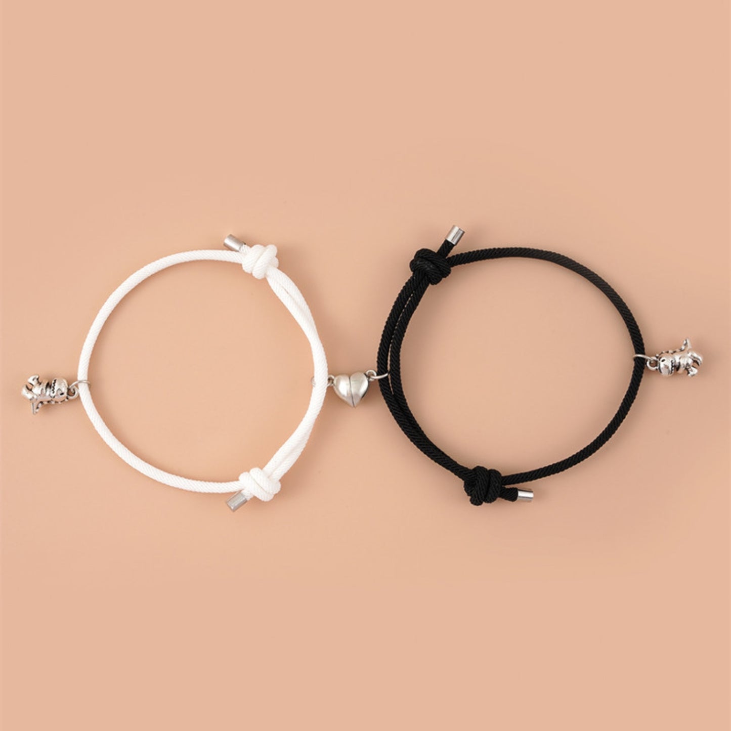 Set of black and white matching adjustable bracelets with silver dinosaur charms and magnetic heart connectors on a peach background.