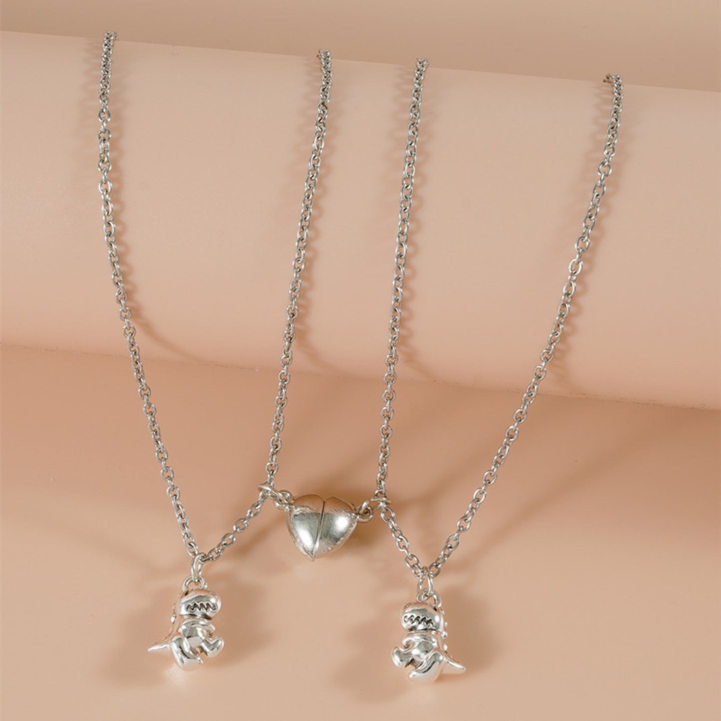 Close-up of silver matching necklaces with magnetic heart and dinosaur charms. Perfect cool friendship necklaces.