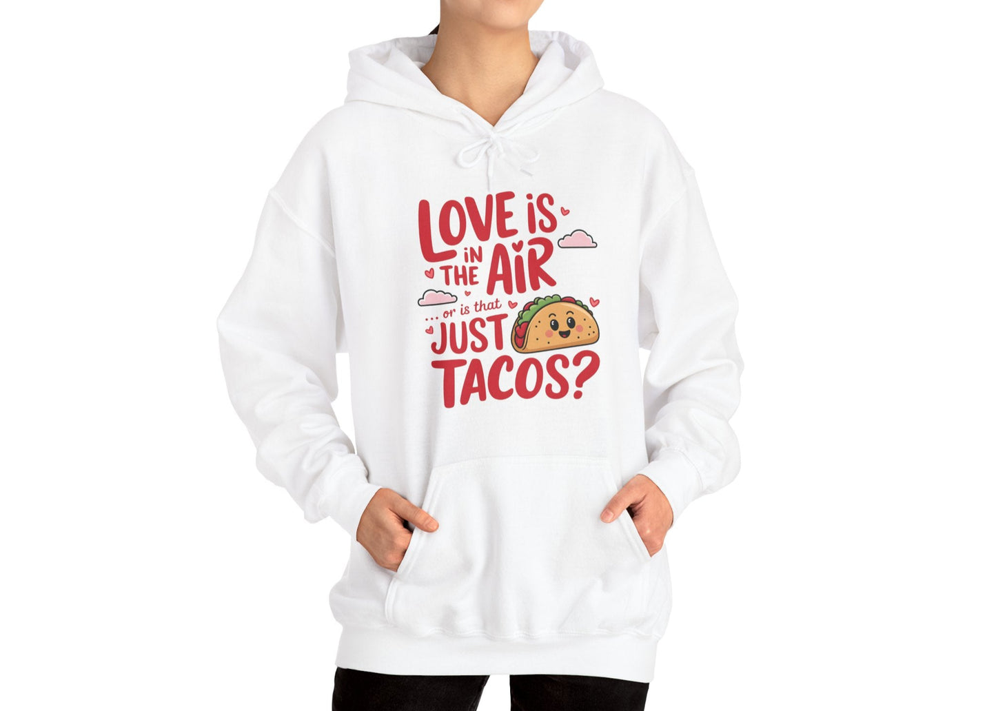 Model wearing a beige hoodie with "Love Is in the Air or Is It Just Tacos?" text and a cute taco graphic in red and yellow while seated. Exclusive release for Valentine's Day. Part of the Vivid Divergence Sensory Friendly Sweaters Range.