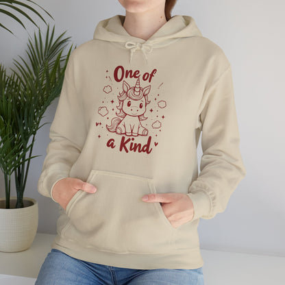 Model wearing a beige hoodie featuring "One of a Kind" text and a cute unicorn design in red while seated. Exclusive release for Valentine's Day. Part of the Vivid Divergence Sensory Friendly Sweaters Range.