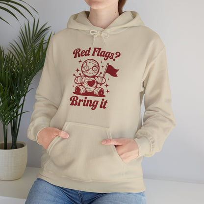 Model wearing a beige hoodie featuring "Red Flags? Bring It" text and a cute voodoo doll holding a red flag while seated. Exclusive release for Valentine's Day. Part of the Vivid Divergence Sensory Friendly Sweaters Range.