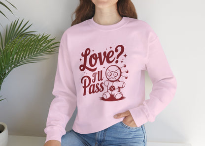 Model wearing a pink sweatshirt with "Love? I'll Pass" text and a cute voodoo doll design in red while seated. Exclusive release for Valentine's Day. Part of the Vivid Divergence Sensory Friendly Sweaters Range.