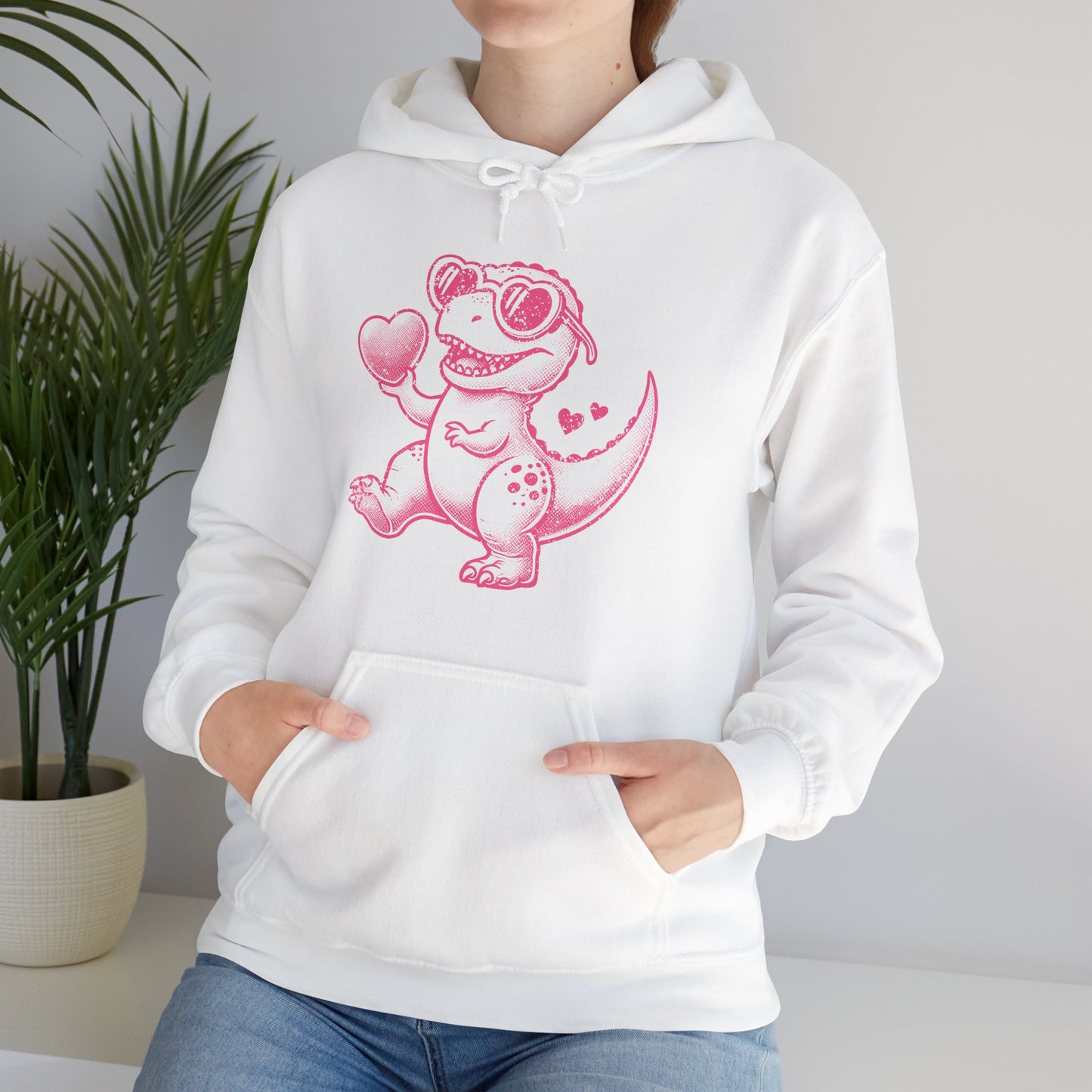 Model wearing a white hoodie featuring a cute cartoon dinosaur holding hearts in a pink design. Exclusive release for Valentine's Day. Part of the Vivid Divergence Sensory Friendly Sweaters Range.