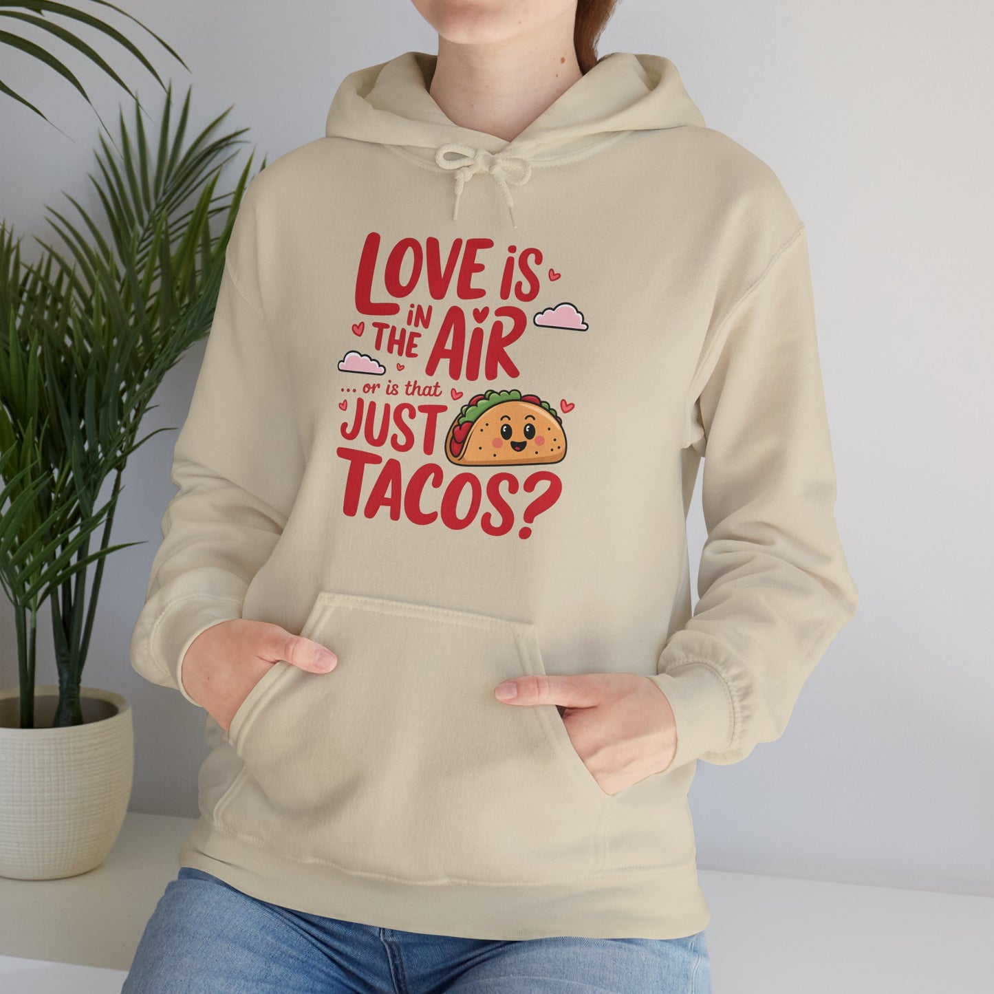 Model wearing a white hoodie with "Love Is in the Air or Is It Just Tacos?" text and a cute taco graphic in red and yellow. Exclusive release for Valentine's Day. Part of the Vivid Divergence Sensory Friendly Sweaters Range.