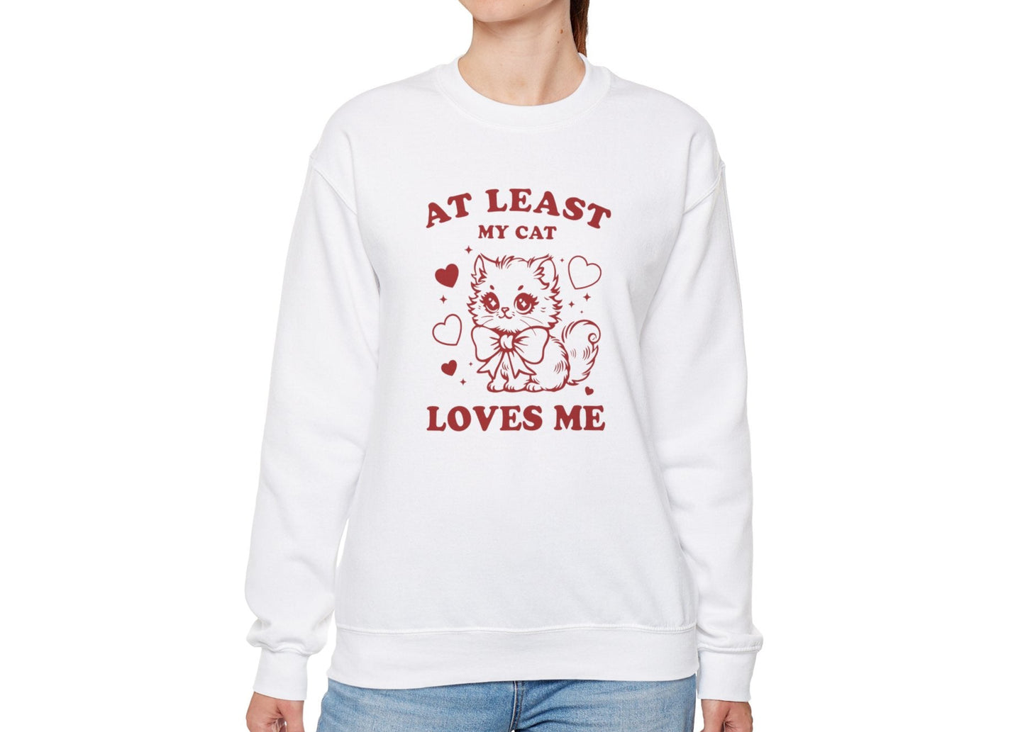 Model wearing a white sweatshirt with "At Least My Cat Loves Me" text and cartoon cat design in red. Part of the Vivid Divergence Sensory Friendly Sweaters Range.