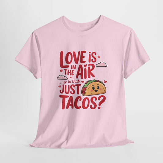 Hanging pink T-shirt featuring red and black text with a taco illustration that reads "Love Is In The Air Or Is It Just Tacos?" Exclusive release for Valentine’s Day. Part of the Vivid Divergence Sensory Friendly Unisex Tees Range.