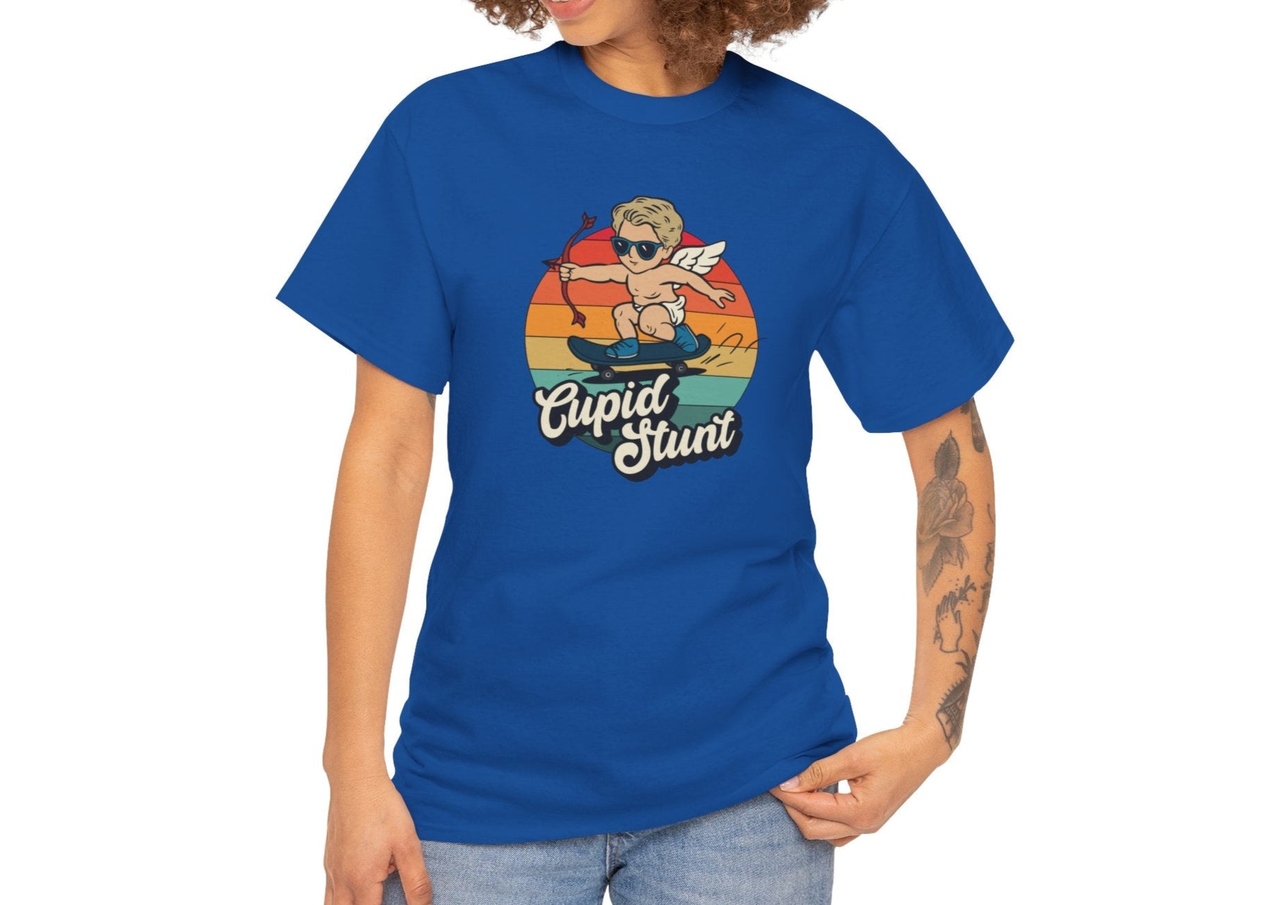 Woman with curly hair wearing a royal blue T-shirt featuring a retro sunset background and a cartoon cupid with the text "Cupid Stunt." Exclusive release for Valentine’s Day. Part of the Vivid Divergence Sensory Friendly Unisex Tees Range.