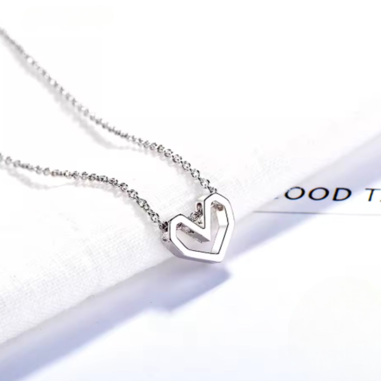 Silver geometric open heart necklace placed on a white fabric background, conveying a sense of simplicity and refined style.