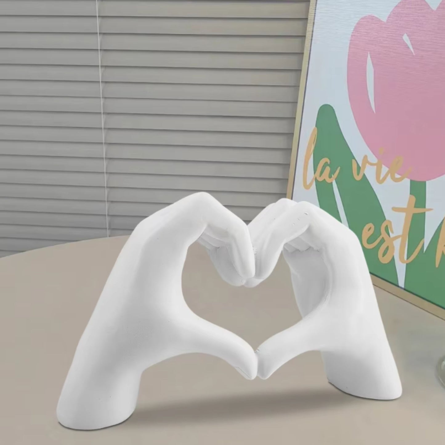 White hand-shaped sculpture forming a heart on a table with a floral wall art piece. Minimalist dopamine decor and a wonderful Valentine's Day gift.