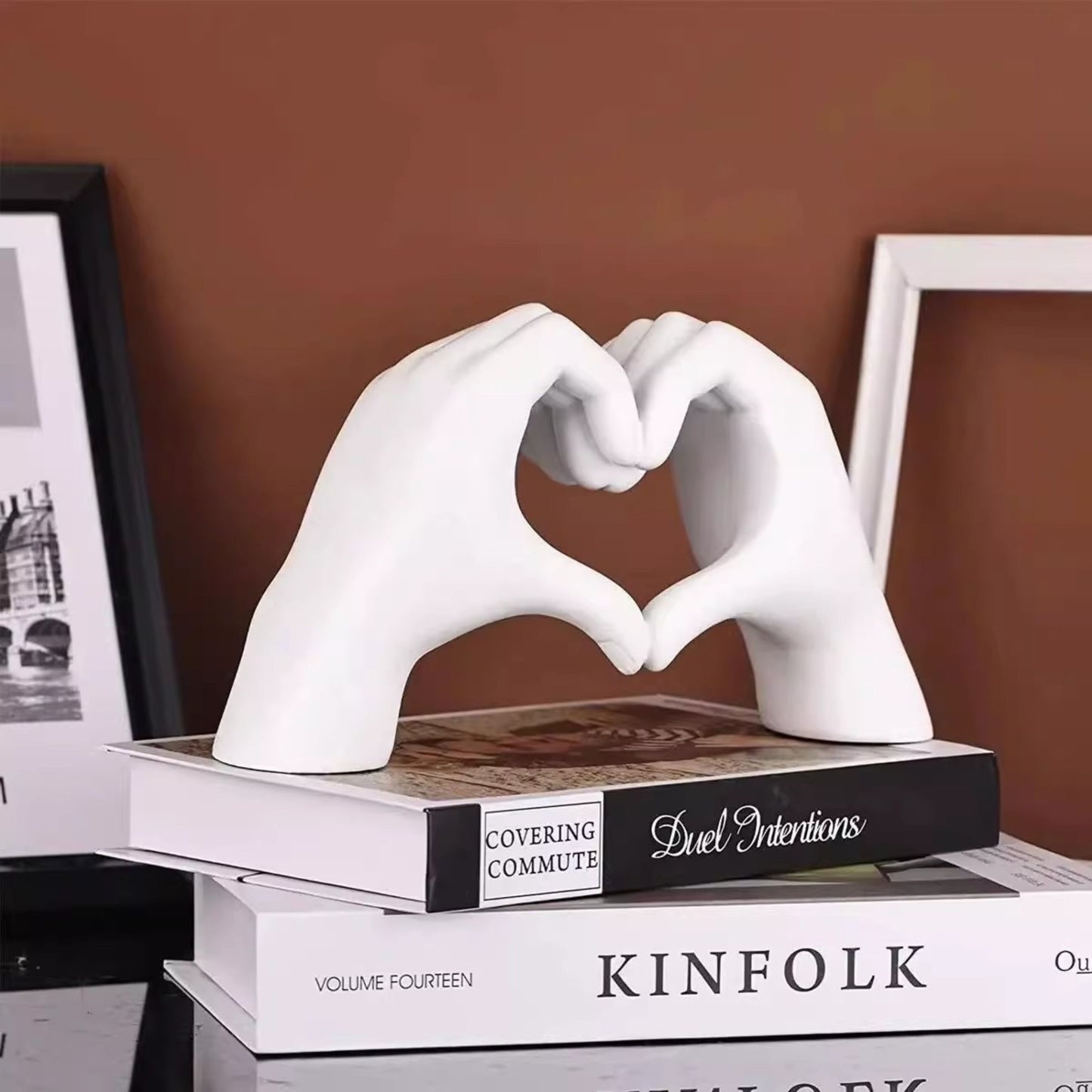 White hand-shaped sculpture forming a heart placed on a stack of books against a brown background. Versatile dopamine decor and a meaningful gift for Valentine's Day.