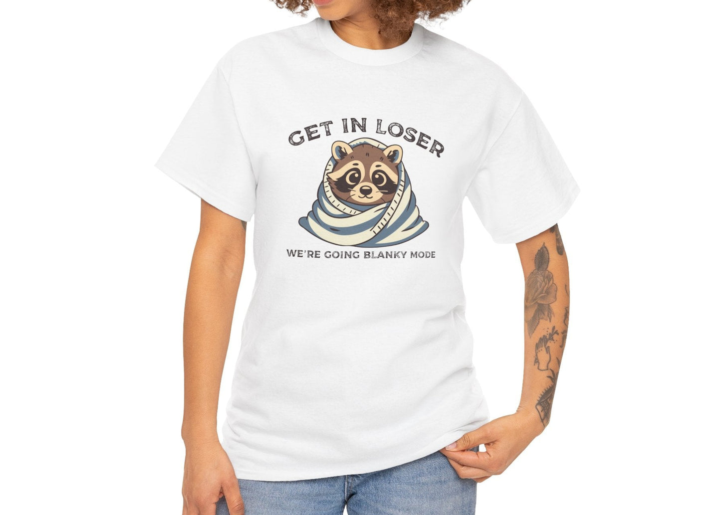 Modeled front view of a white T-shirt featuring a cute raccoon wrapped in a blanket with text that reads "Get In Loser, We're Going Blanky Mode." Part of the Vivid Divergence Sensory Friendly Unisex Tees Range.