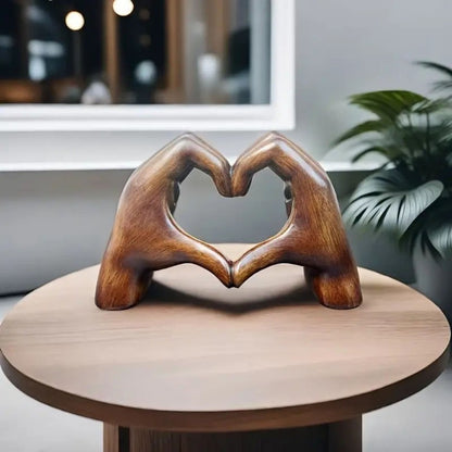 Wooden look hand-shaped sculpture forming a heart on a round wooden table, with plants and a modern interior in the background. A stunning piece of dopamine decor and a thoughtful gift for Valentine's Day.